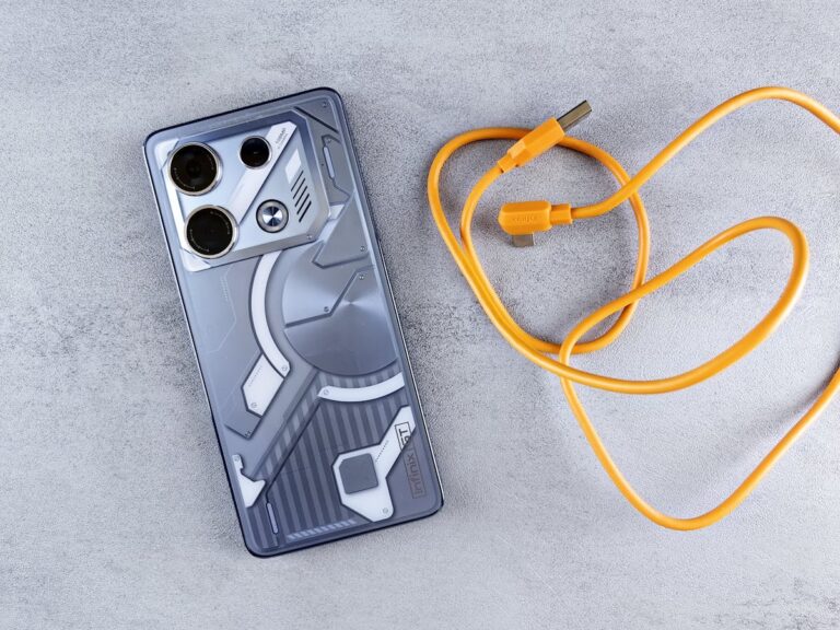 A sleek smartphone beside a bright orange charging cable on a textured surface.