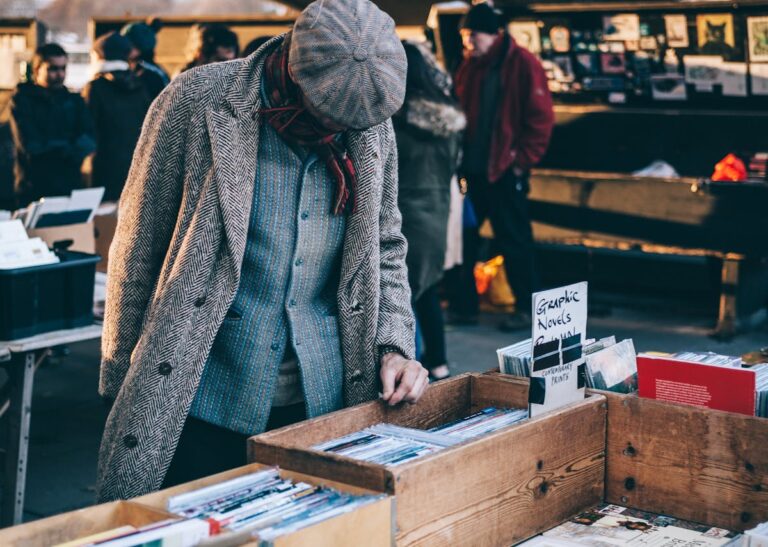 A man in vintage clothing browses through books at an outdoor market.